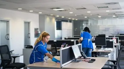 two workers cleaning an office following tasks listed on an office cleaning checklist