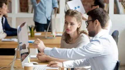 a manager discussing training items to a new employee using a new employee training checklist on a desktop