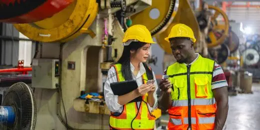 un supervisor de fabricación comentando ejemplos de evaluación de riesgos a un empleado durante una evaluación práctica de riesgos en el lugar de trabajo