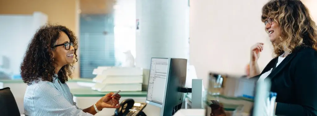 a receptionist assisting a visitor using a visitor management software on a desktop