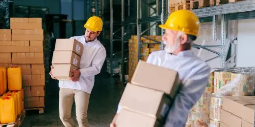 two workers encountering ergonomic hazards at work while carrying and transferring boxes in a warehouse